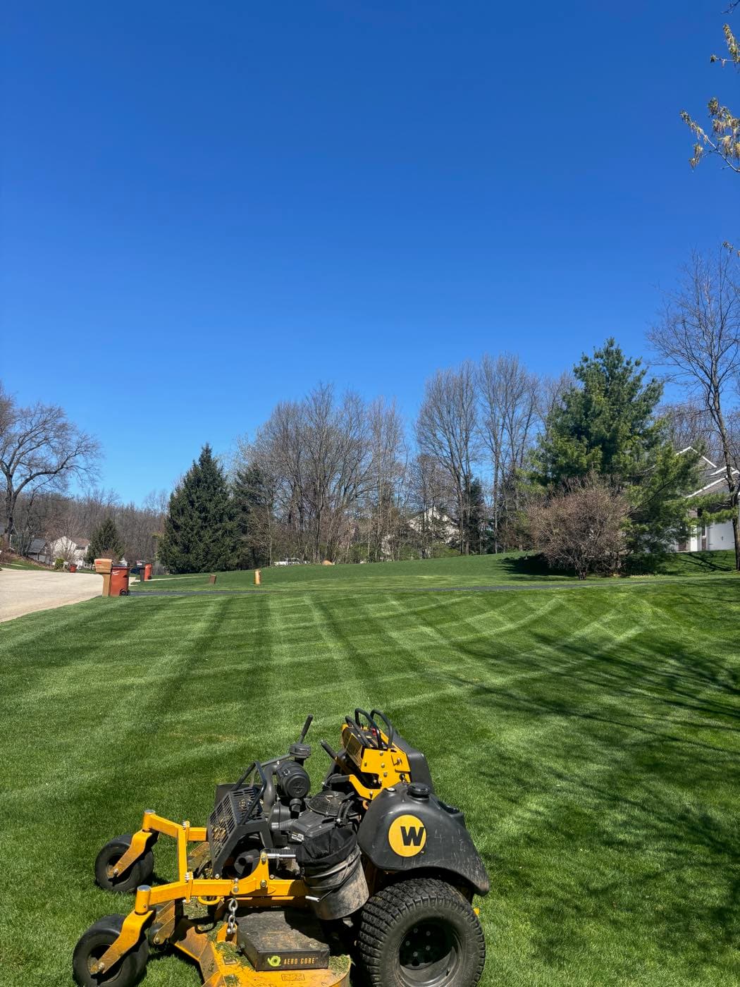 Commercial-grade stand-on mower cutting crisp stripes across a large open property